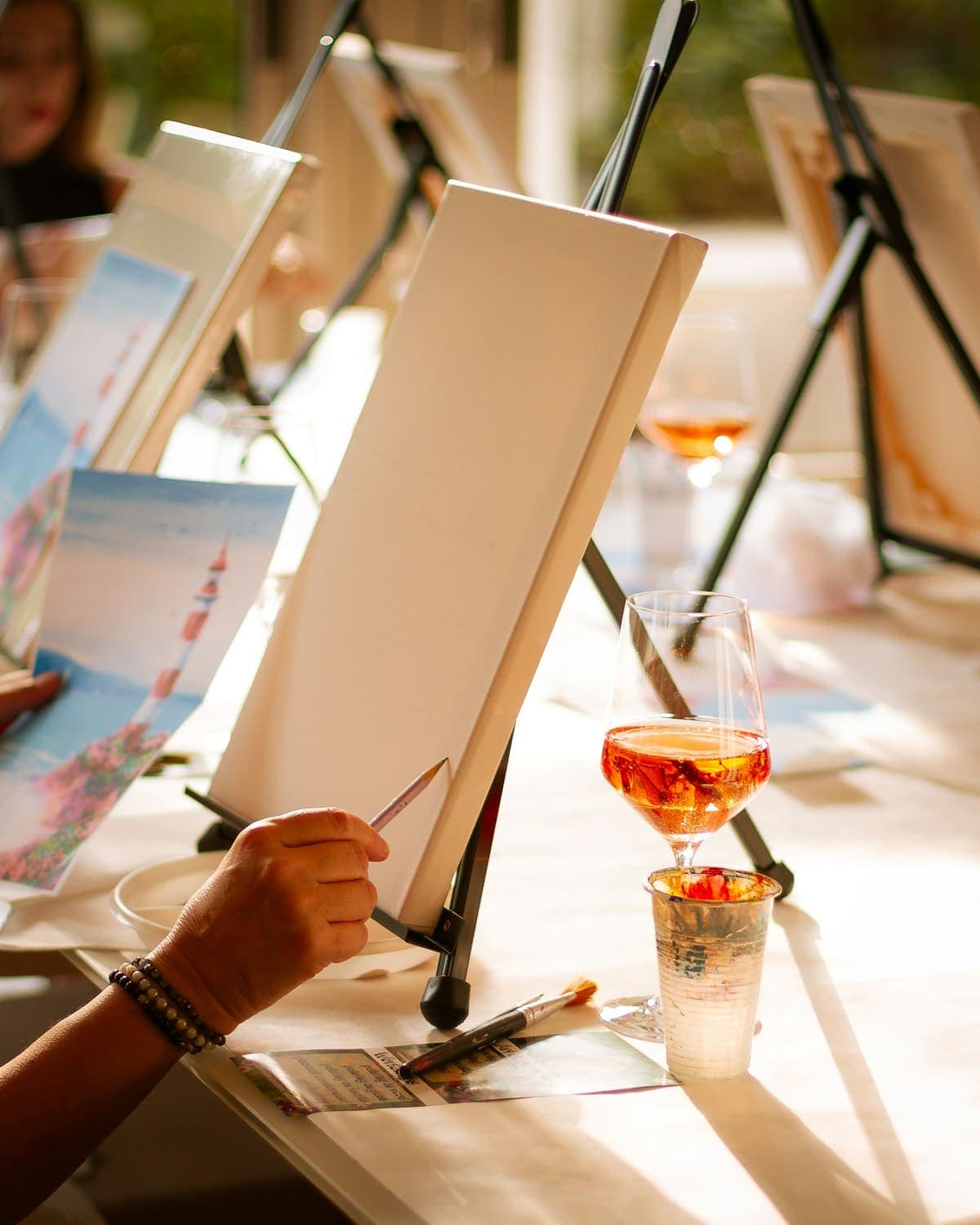 People painting at easels with glasses of wine